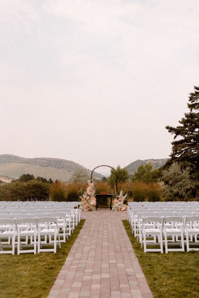 The Manor House in Colorado is one of the best Colorado wedding venues. This ceremony view is set with white chairs and boho florals on the arch.