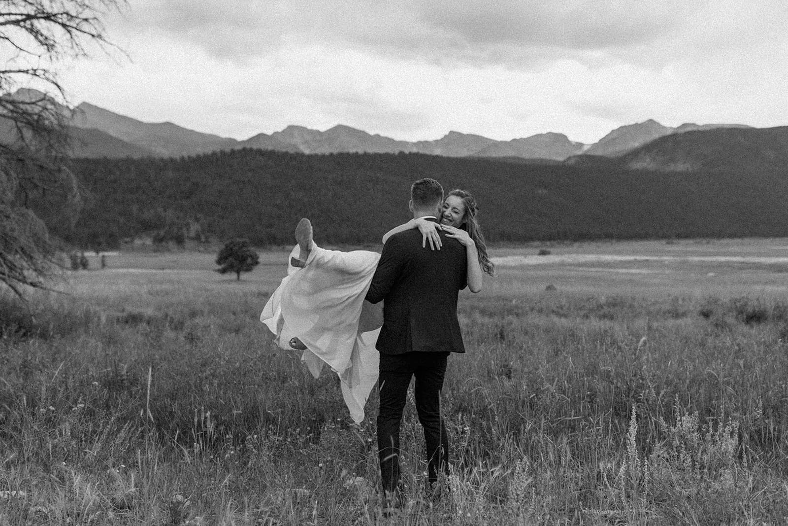 Man and woman embracing in a field next to the mountains on their elopement day.