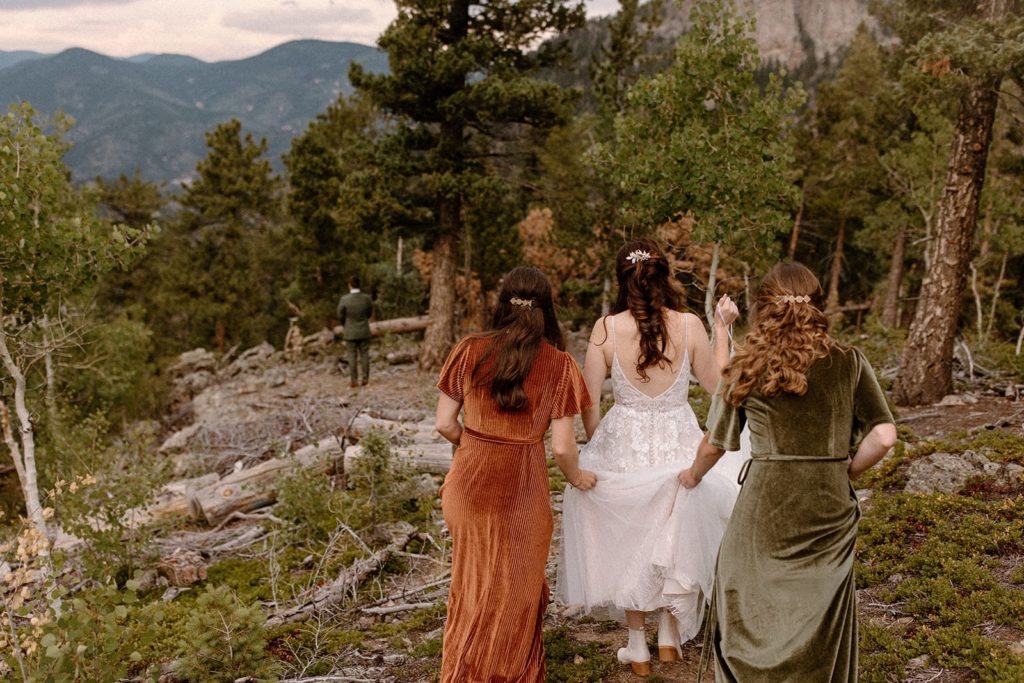 bridesmaids holding the dress of their bride while she walks down to her fiance for a first look at their North Star Gatherings Wedding