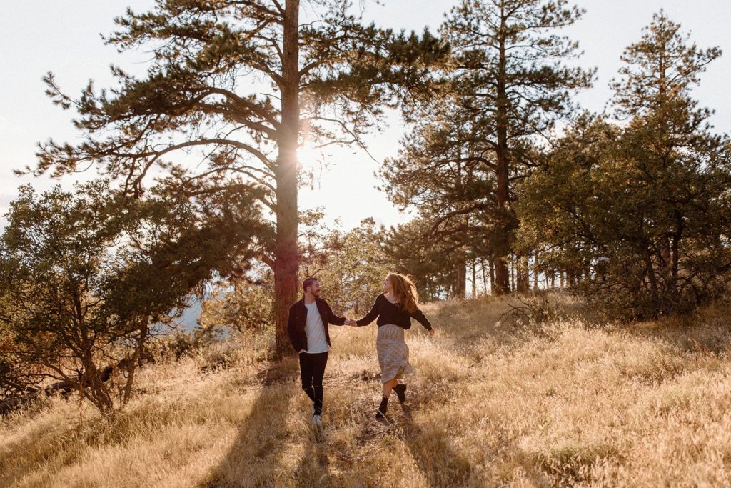 man and woman running through a field with trees for Mountain Engagement Photos