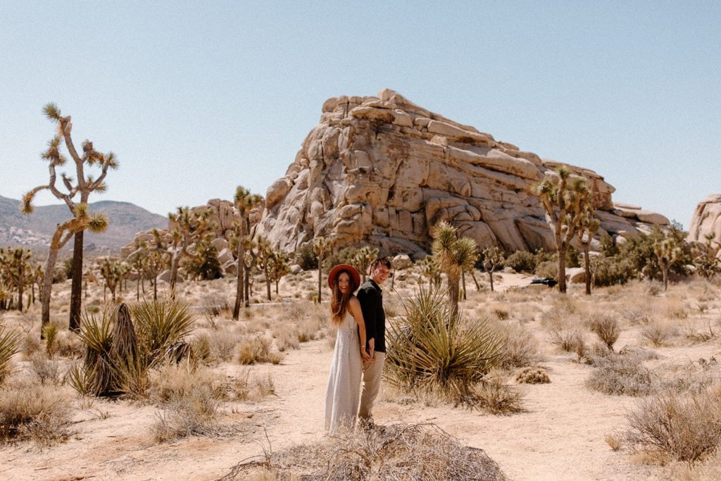 man and woman standing back to back in front of a large rock in Joshua Tree National Park